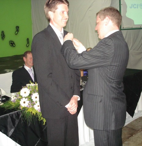 Jornalista Joni Leocir Lang recebendo o pin de presidente da JCI Marechal Cândido Rondon de seu antecessor Gelson José Linck, EM DEZEMBRO DE 2009. 
Imagem: Acervo pessoal - FOTO 15 -