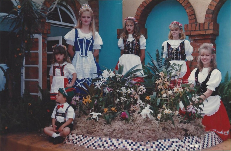 Vitrine de plantas em flor para a gravação do vídeo-tape para anúncio na televisão da 3ª Oktoberfest e da 1ª Exposição de Orquídeas e Plantas Ornamentais de Marechal Cândido Rondon. 
A menina à direita é Marise Schöne. As outras nãoidentificadas. 
Imagem: Acervo Memória Rondonense