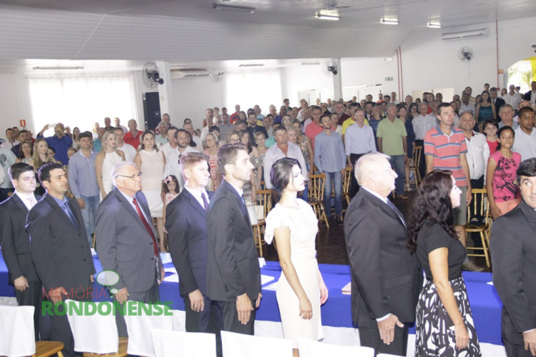 Momento da entoação do Hino Nacional na abertura da sessão solene de posse. 
Da esquerda a direita: vereador Arion Nasighil, vereador Adriano Backes, vereador Pedro Rauber, vereador Nilson Hachmann, prefeito eleito Márcio Andrei Rauber, Josiane Laborde Rauber, vice-prefeito Ilário Hofstetter, Márcia Veit e o vereador Adriano Cóttica. 
Imagem: Acervo Memória Rondonense - Crédito: Tioni de Oliveira