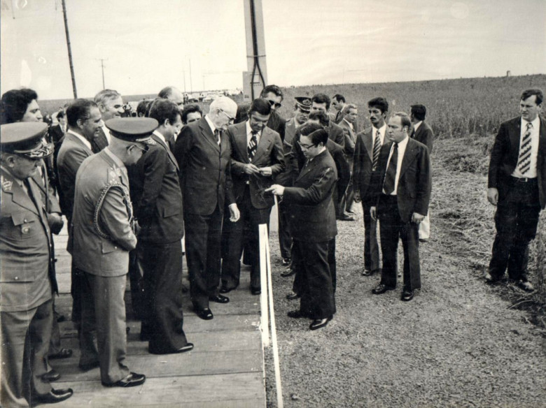 Ministro Shigeaki Ueki mostrando ao Presidente Geisel o enraizamento de um pé de soja. 
Da esquerda a direita, na primeira fila: 1º - militar não identificado; 2º - Ministro Hugo de Abreu;  3º - ministro Alysson Paulinelli; 4º - Presidente Ernesto Geisel;  5º - governador Jayme Canet Júnior; e 6º - ministro Shigeaki Ueki. 
Na segunda fila: 1º - deputado estadual Werner Wanderer; 2º - ministro da Educação, Ney Braga; 3º - prefeito municipal Almiro Bauermann;  4º -  Paulo Carneiro Ribeiro, secretário de Agricultura do Paraná (careca); e demais não identificados. 