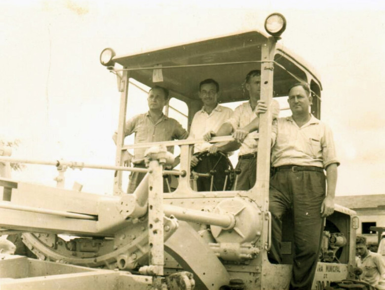 Outro momento do desfile da primeira patrola por ruas da cidade. 
Na gabinete da  máquina, da esquerda a direita, vereador Helmuth Priesnitz, presidente da Cãmara Municipal; prefeito municipal Arlindo Alberto Lamb; vereador Harry Pydd e vice-prefeito Alfredo Wanderer. 
Imagem: Acervo familia Arlindo e Norma Lamb