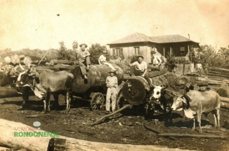 || Pátio de toras da serraria do pioneiro Alberto Lettnin, que ficava atrás do Hospital Marechal Rondon, à Rua Espírito Santos. O primeiro proprietário dessa serraria foi o pioneiro Rinaldo Ludwig. As duas toras que estão sob as duas carroças foram beneficiadas e a madeira serviu para a construção da primeira residência da família Lohmann. No meio das duas carroças, é o pioneiro Artur Lohmann. A residência que aparece ao fundo, revitalizada, é hoje (18.07.2017) a residência do empresário Paulo Rempel. A fotografia é de 1957. Imagem: Acervo Edeltraud Steinmacher Lettnin