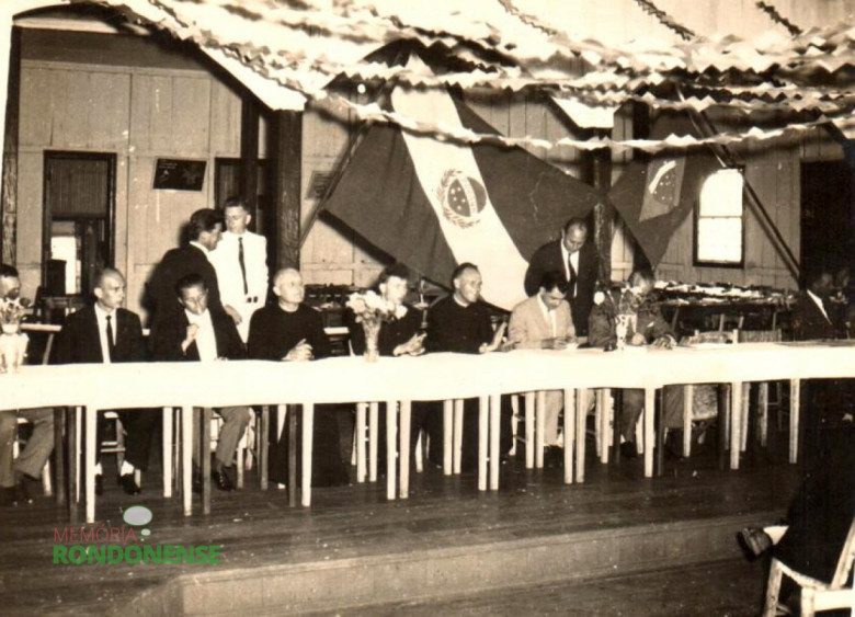 Autoridades sentadas à Mesa de Honra da solenidade de posse de Arlindo Alberto Lamb, como primeiro prefeito eleito de Marechal Cândido Rondon. 
       Da esquerda para a direita: a 4ª pessoa é o Pe. Aloísio Baumeister, vigário da Paróquia Nossa Senhora da Glória , Quatro Pontes, e em seguida o pastor Joachim Pawelke, da Comunidade  Martin Luther. As demais pessoas da mesa não identificadas. 
Imagem: Acervo idem 
