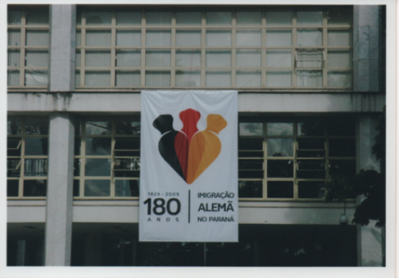 Banner dos 180 anos da Imigração Alemã no Paraná afixado numa das janelas do centro cultural da Assembleia Legislativa do Estado do Paraná.