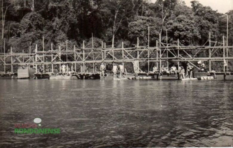 Grupo de trabalhadores junto a estrutura de construção da ponte. 
