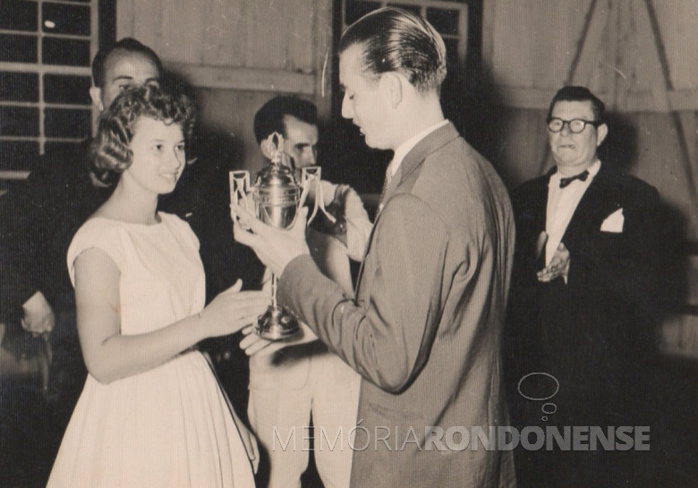 A jovem pioneira Lori Koch recebendo a taça do pioneiro Arno Roesler. 
Não se descobriu o motivo da entrega do troféu. 
Á direita, Willy Carlos Trentini, primeiro cartorário de Marechal Cândido Rondon .