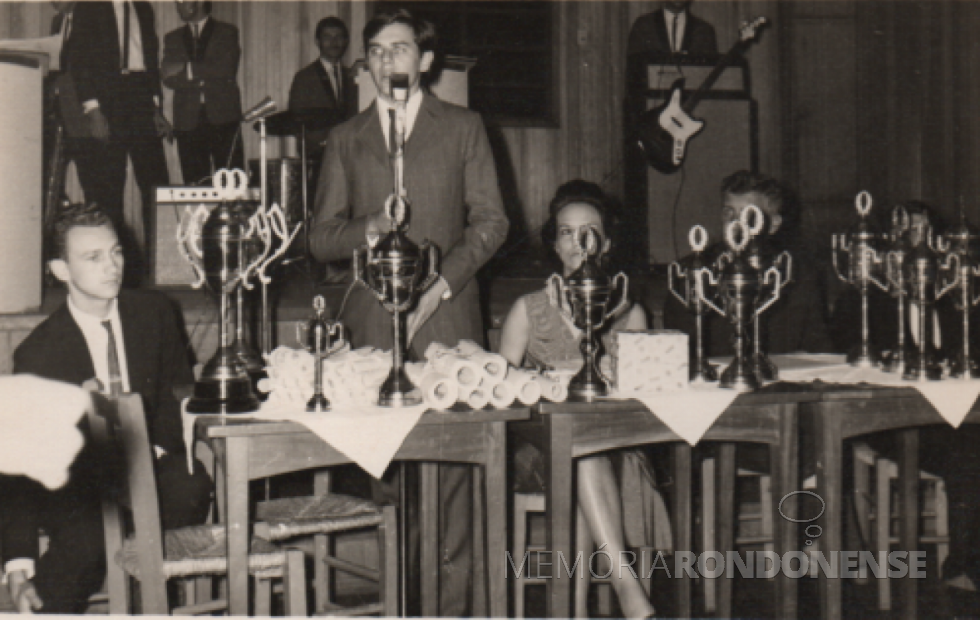 || Estudante rondonense Elio Edvino Winter, presidente da Associação Rondonense de Estudantes Secundários (ARES), presidindo a cerimônia de entrega da premiação às equipes vencedoras dos Jogos da Primavera 1969. 
Ao seu lado direito, Gerade Reuter; e à esquerda, a professora Idalina Vianna Guzzoni. 
Imagem: Acervo Elio Winter - FOTO 13 -