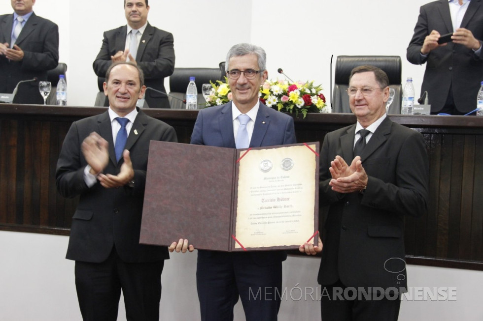 || Tarcísio Hübner recebendo a comeda da Medalha Willy Barth, em sessão solene da Câmara Municipal de Toledo (PR), em maio de 2018. À sua direita, Lúcio de Marchi, prefeito municipal de Toledo; e à sua esquerda, vereador Renato Reimann, presidente da Câmara Municipal.
Imagem: Acervo Comunicação do Município de Toledo - FOTO 17 -