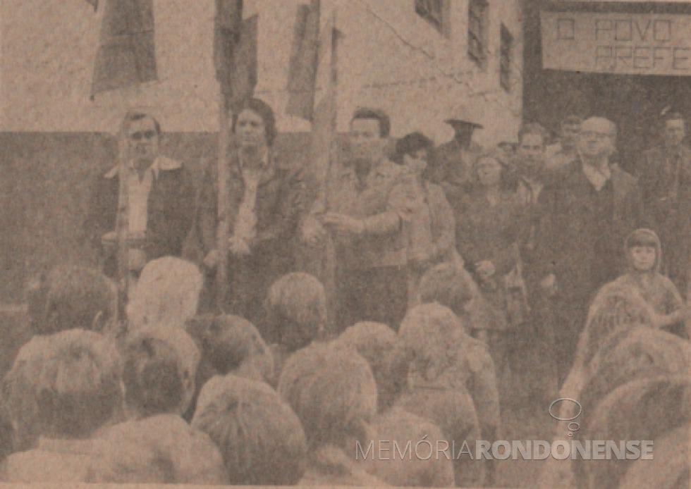 || Hasteamento das bandeiras na instalação da Administração Municipal de Marechal Cândido Rondon, na sede distrital de Margarida, em agosto de 1978.
Hasteiam as bandeiras: prefeito municipal Verno Scherer (e), deputado estadual Werner Wanderer (c) e Germano José Kuhn (pioneiro do distrito rondonense citado. Ao fundo, de óculos, padre Vitoldo Kosicki, pároco da Paróquia Santa Margarida.
Imagem: Acervo Família Ariovaldo Luiz Bier/Projeto Memória Rondonense - FOTO 8 -