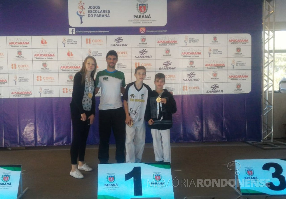 || Atletas rondonenses ganhadores da medalha de ouro no taekwondo, na fase final dos Jogos Escolares do Paraná 2018. 
Da esquerda à direita: Maria Eduardo Arndt Fritschi, treinador professor Pedro Alencar, atleta Julio César e medalhista de ouro Esdras Furmanovicz. 
Imagem: Acervo Imprensa PM-MCR - FOTO 9 -