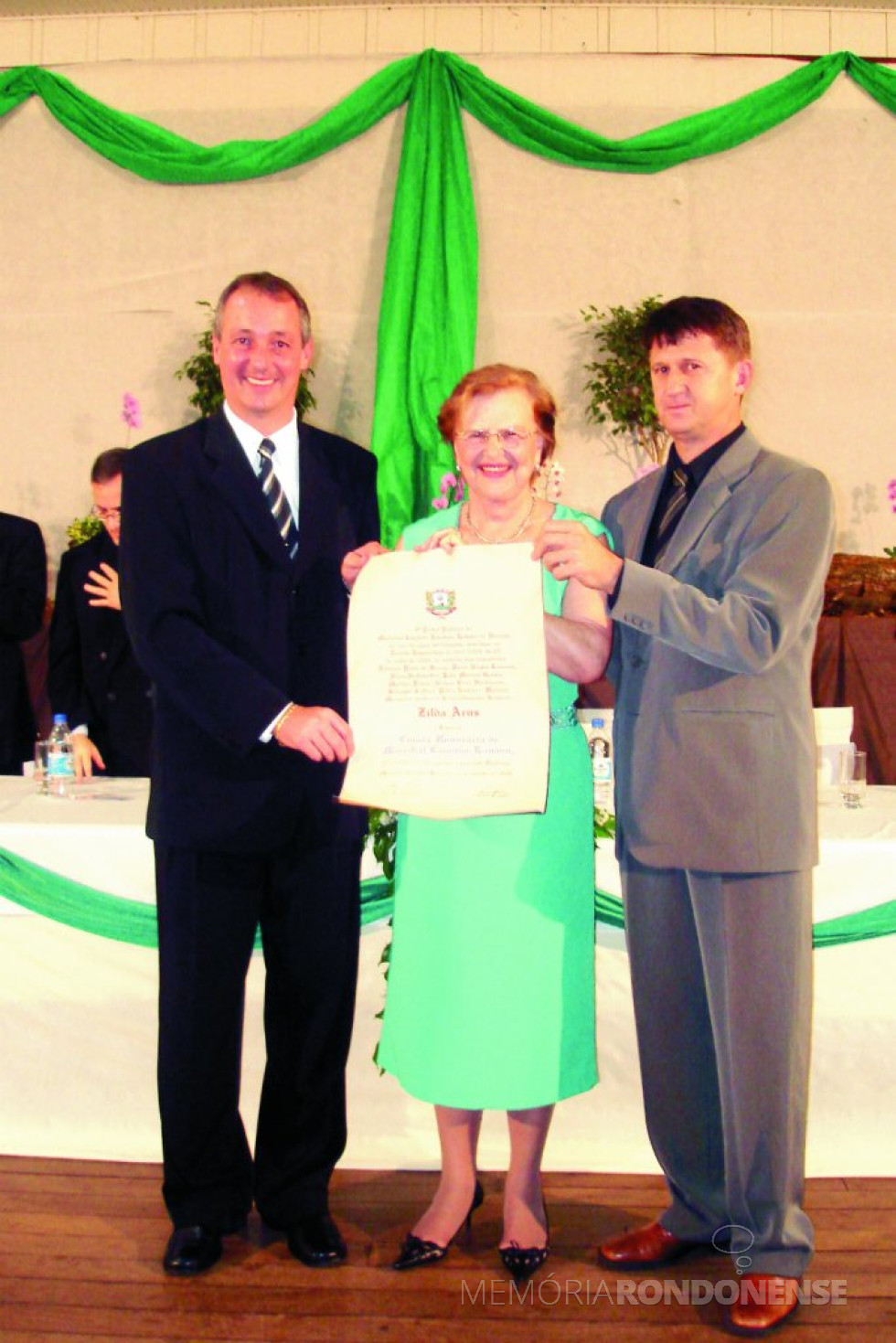 || Zilda Arns Neumann recebendo o título de cidadã honorária de Marechal Cândido Rondon, em agosto de 2006, tendo à sua direita, o prefeito municipal Edson Wasem e à esquerda o vereador Nilson Hachmann, proponente da homenagem.
Imagem: Acervo Memória Rondonense - FOTO 7 -