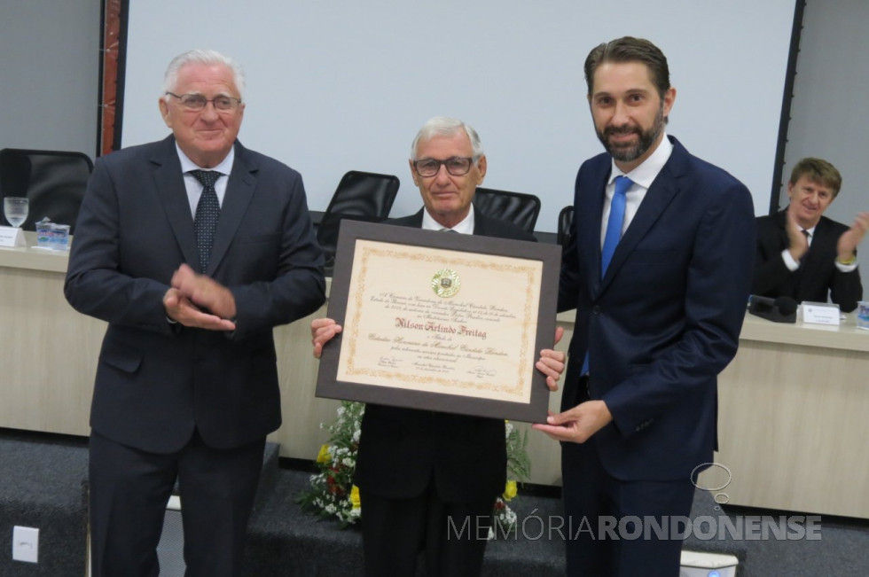 || Professor Nilson Arlindo Freitag com o título de cidadão honorário de Marechal Cândido Rondon, em dezembro de 2018, ladeado pelo vereador Pedro Rauber (e), autor da homenagem, e pelo prefeito municipal Marcio Andrei Rauber.
Imagem: Acervo Imprensa CM-Marechal Cândido Rondon - Crédito: Cristiano Marlon Viteck - FOTO 24 -
