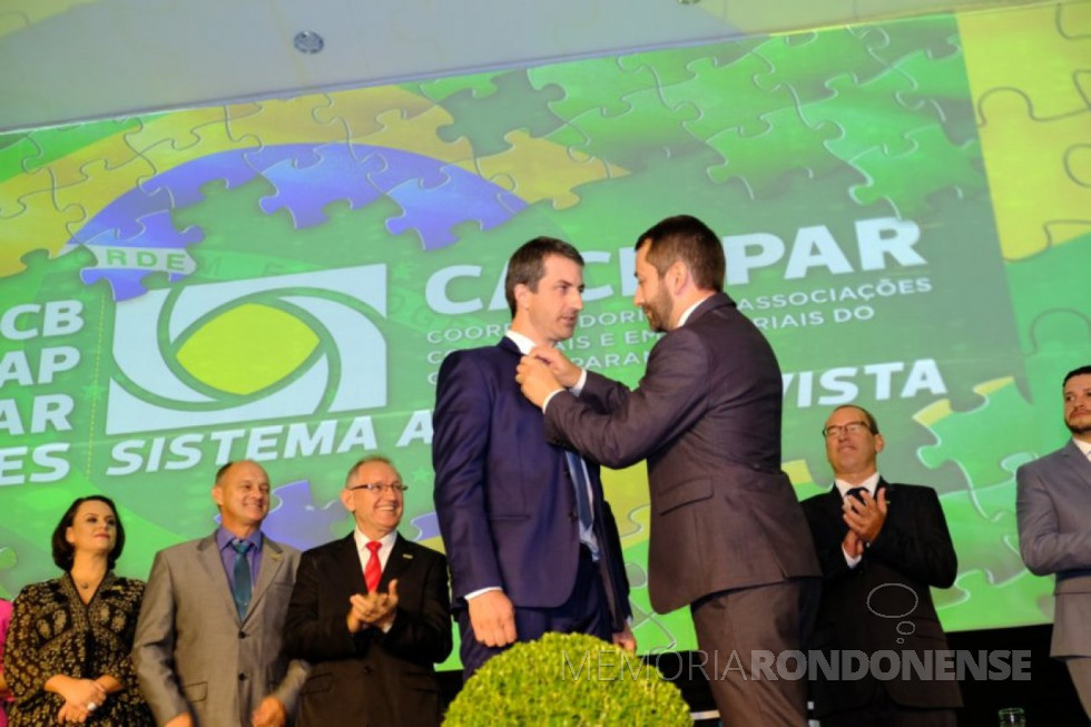 || Empresário Alci Rotta Junior recebendo o boton da presidência da Caciopar de seu antececessor Leorevaldo Curtarelli de Oliveira, em abril de 2018.
Ao fundo, da esquerda a direita: 1ª - não identificada; 2ª - empresário Reinaldo Scherer, de Pato Bragado; 3ª empresário Reni Fernando Felipe; 4ª e 5ª - não identificadas.
Imagem: Acervo O Presente - FOTO 17 -