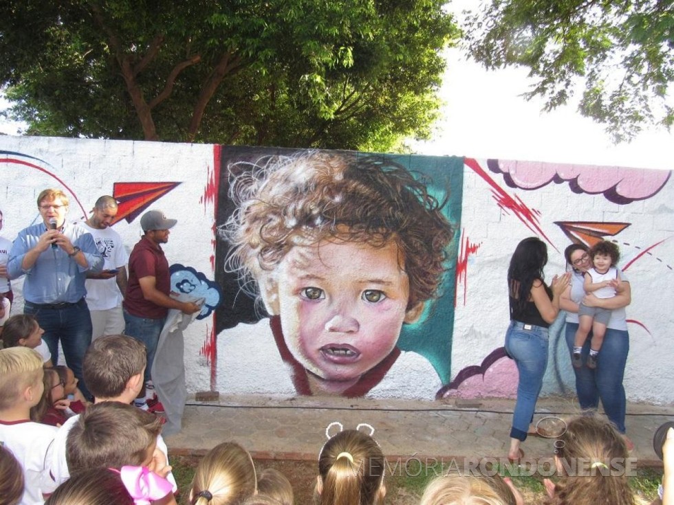 || Solenidade de apresentação da grafitagem do muro junto ao Colégio Luterano Rui Barbosa, em fevereiro de 2018.
À esquerda, o diretor Carlos Krache com  os dois grafiteiros e a aluna retratada. 
Imagem: Acervo do Colégio - FOTO 12 - 