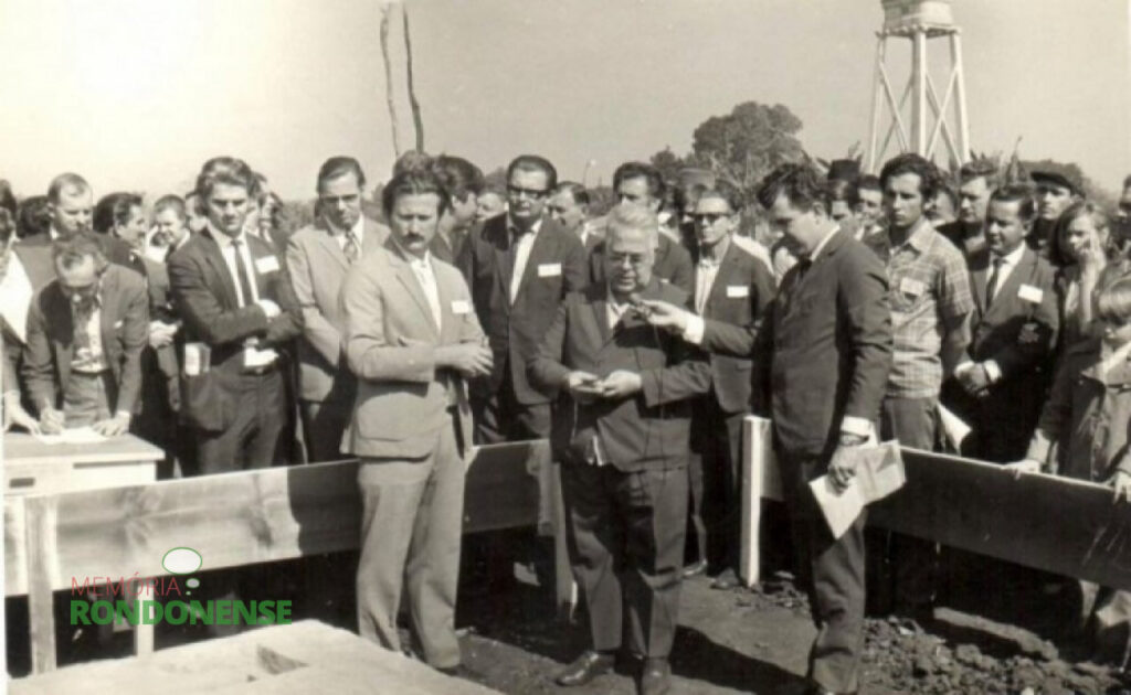 Lançamento da pedra fundamental do setor administrativo na atual sede central da Copagril. Na foto, da esquerda para a direita: atrás da pessoa que está assinado o livro de presenças, o vereador Hasrry Pydd; ao lado esquerdo da pessoa com a cabeça virada, o vereador Harry Feiden; a equerda da pessoa que está assinando, o engenheiro-agronômo Felipe Laginski (de terno preto e gravata); no centro, de óculos e terno preto e gravata, Plínio Kleemann, primeiro diretor-secretário da Copagril e atrás dele, o sr. Arlindo Alberto Lamb, primeiro diretor-presidente da Copagril; e mais a direita, de óculos, o pioneiro rondonense e agricultor Emilio Pedde; dentro do esquadro de construção, as esquerda o locutor Vitorino Angeli, da Rádio Difusora. o padre Antonio Darius procedendo a benção da futura sede; e em seguida, o médico-veterinário Leopoldo Piotrowski, do Sindicato Rural Patronal de Marechal Rondon e anos depois diretor-presidente da Copagril (Imagem: Acervo Cleci Kleemann/Clarice Dahmer).