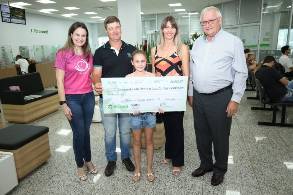 || Luiz Carlos Podkowa, esposa e filha ladeados por Sandra Wagner Serra (d), gerente da agência Sicredi PR/SP D. João VI e  Adolfo Rudolfo Freitag. diretor -presidente da Sicredi Aliança PR/SP, em outubro de 2018.
Imagem: Acervo da cooperativa de crédito - FOTO 25 -