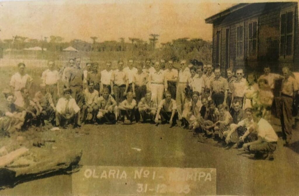 || Pioneiro toledano Ondy Helio Niederauer (de óculos escuros), na companhia de funcionários da colonizadora Maripá e filhos destes que ajudaram na cobertura de sua residência com as primeiras telhas fabricadas pela olaria instalada no atual município de Pato Bragado.
Imagem: Acervo Museu de Pato Bragado - FOTO 10 -