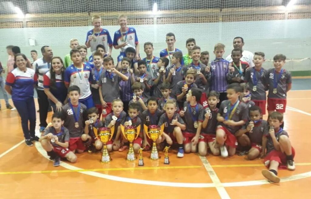 || Equipes de futsal campeãs da Copa da Amizade de Futsal 2018,  em setembro de 2018, na companhia  da secretária de Educação, Cultura e Esportes, Araceli Basso Tauchert (e); equipe do Departamento de Esportes de Quatro Pontes  e o técnico Edevaldo de Moura (Mico, à direita). 
Imagem: Acervo Imprensa PM-Quatro Pontes - FOTO 19 -